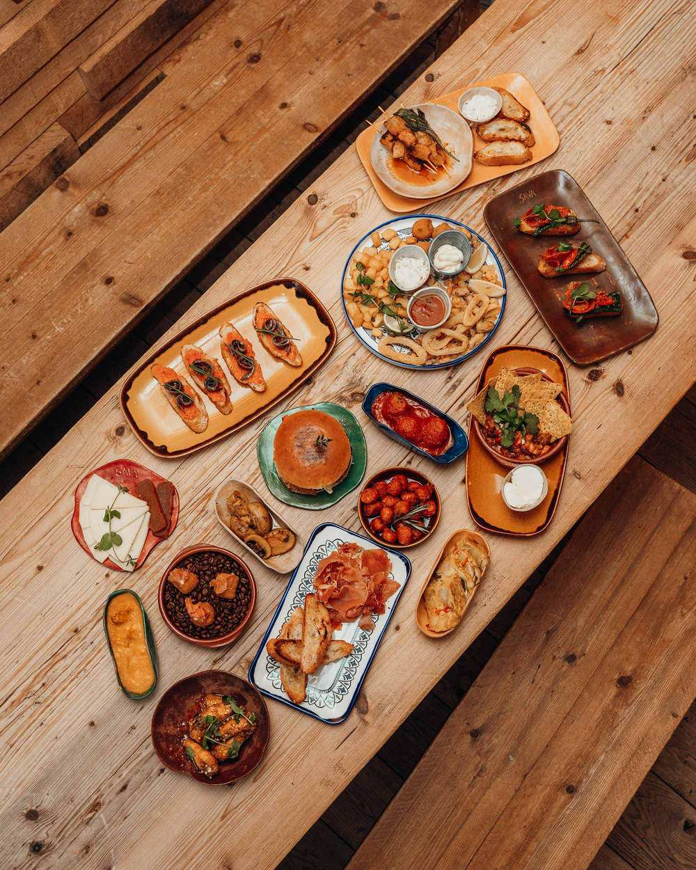 Bovenaanzicht van een uitgebreide tapasselectie op een houten tafel bij Sava