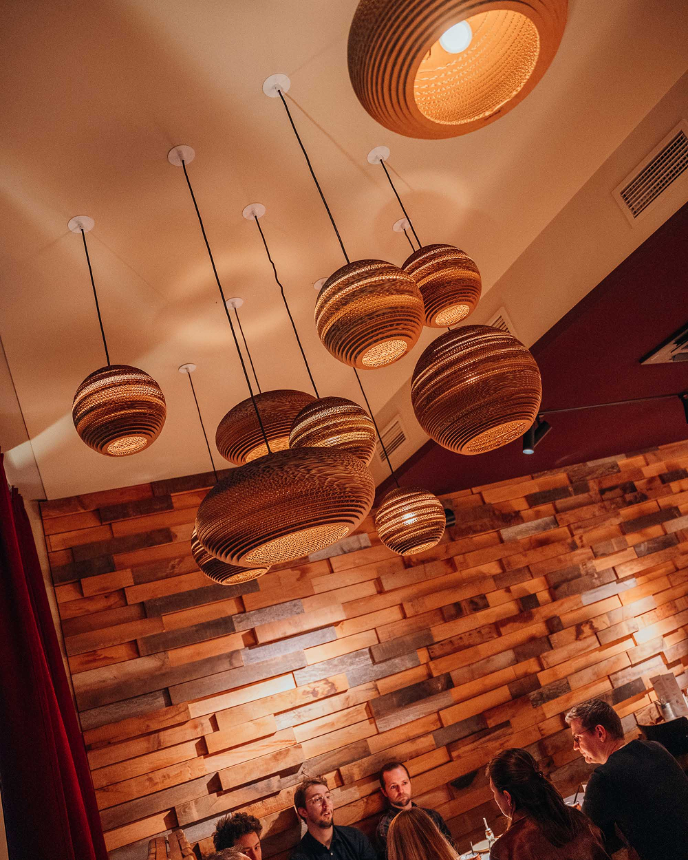 Sfeerverlichting met design-hanglampen boven de houten wand bij Sava