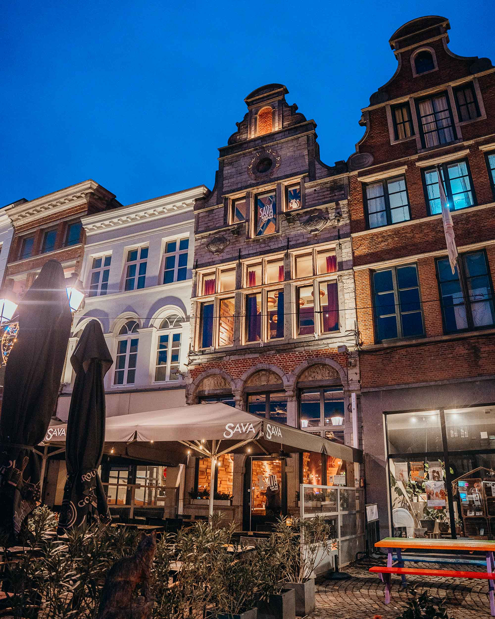 Verlichte gevel van tapasbar Sava in het historische pand De Kat aan de Grote Markt in Mechelen bij avond