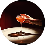 Hands pouring a red cocktail into a coupe glass