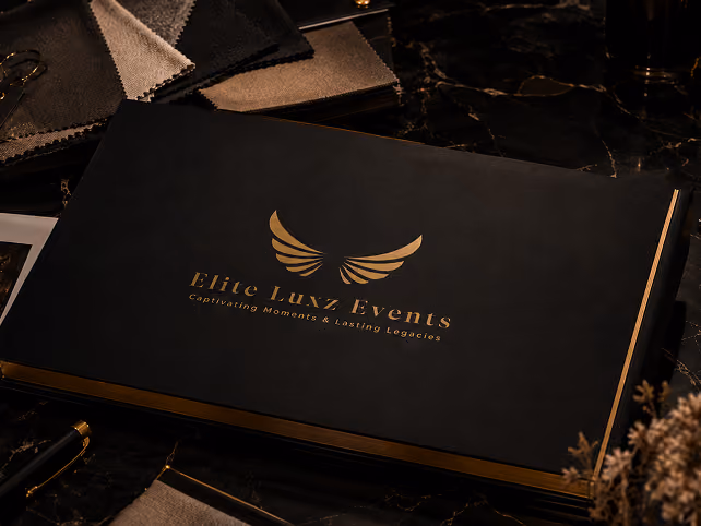 Elite Luxz Events branded portfolio book with gold wing logo beside fabric swatches and a pen
