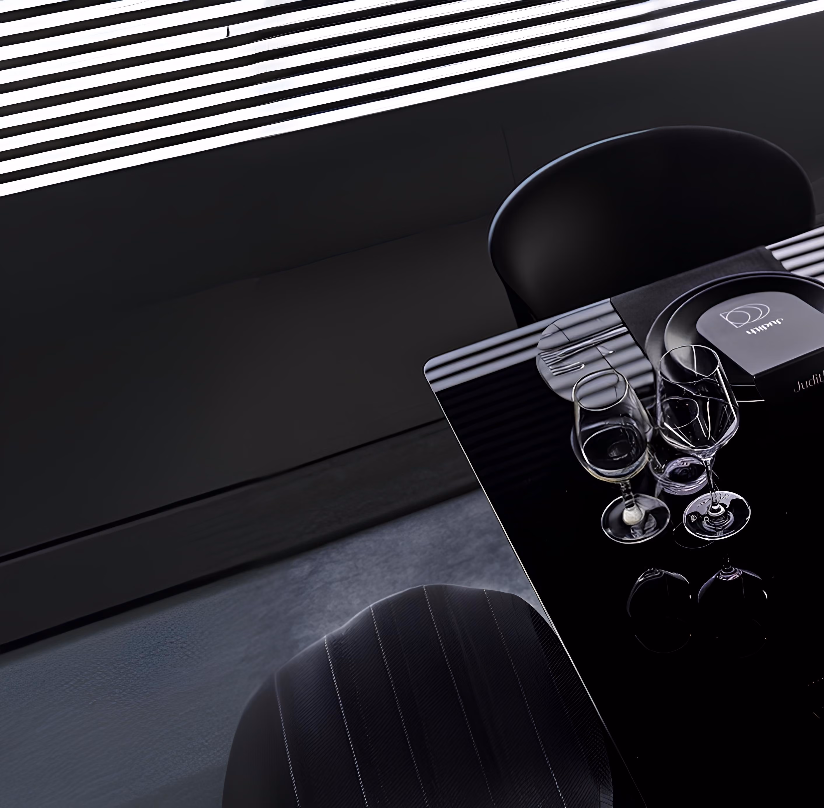 Dark, modern table setting with wine glasses under dramatic diagonal light beams