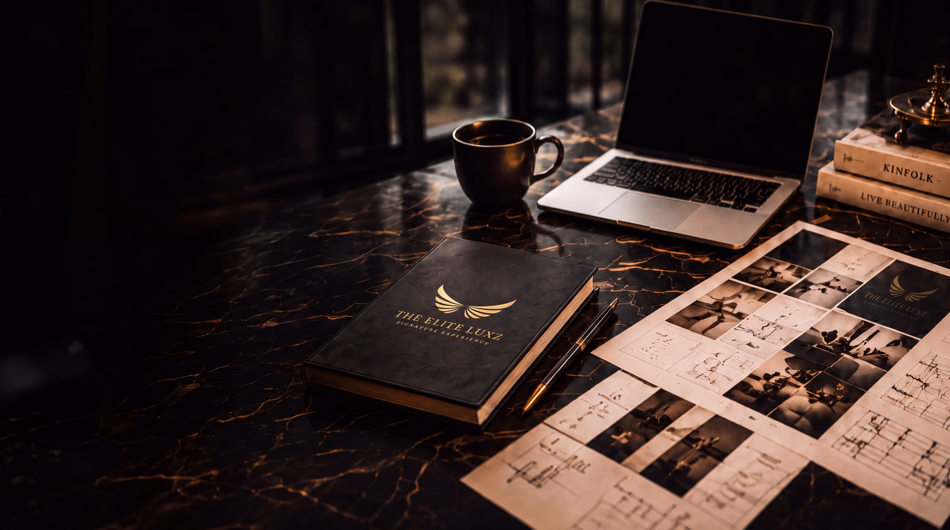 Dark marble desk with a closed book, pen, coffee cup, laptop, books, and photo sketches.
