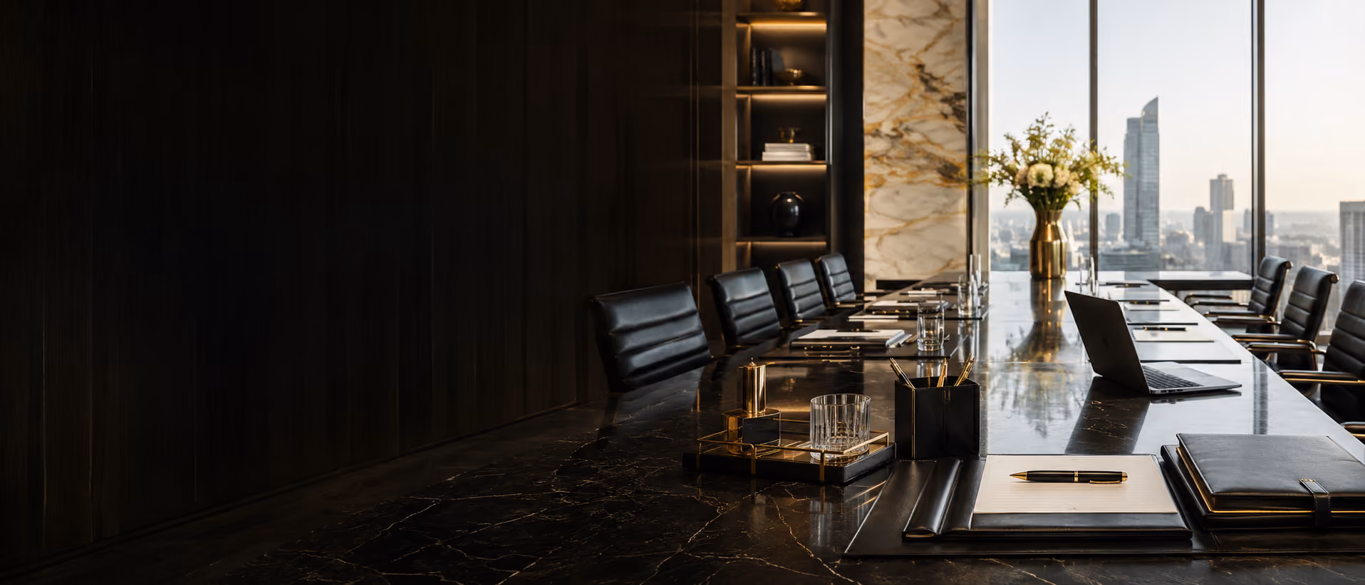 Modern conference room with a long marble table, black chairs, laptop, and city skyline view.