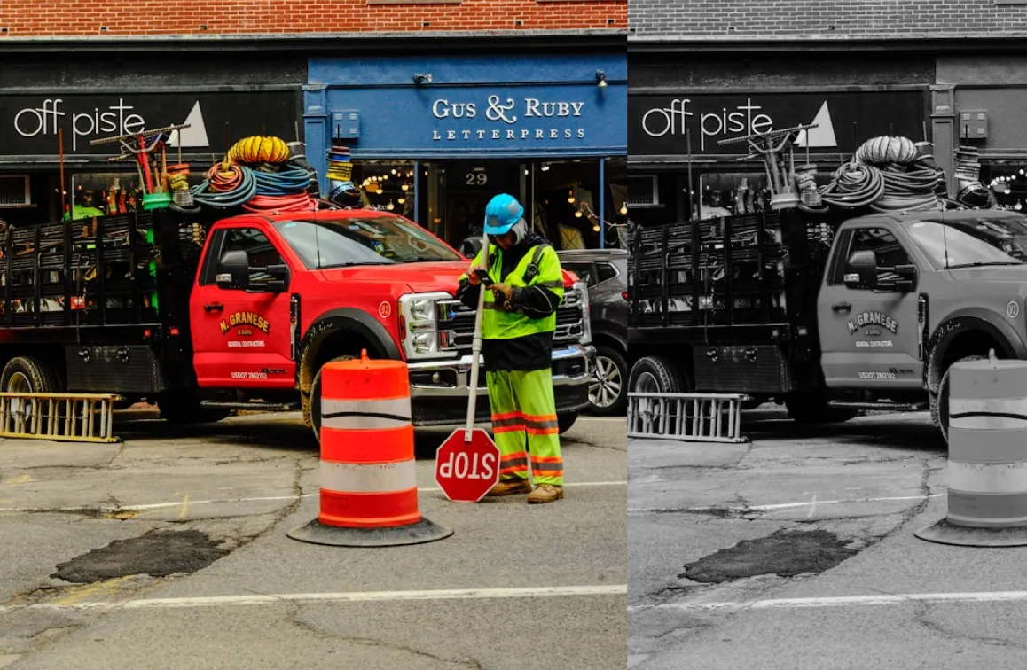 Construction worker in safety gear holding a stop sign near orange traffic barrel by a red utility truck.