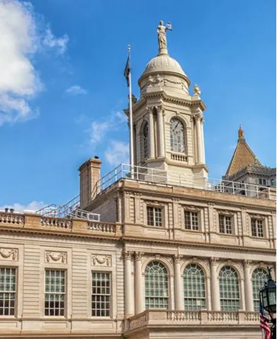 Historic building with ornate windows and a tower topped by a statue under a blue sky.
