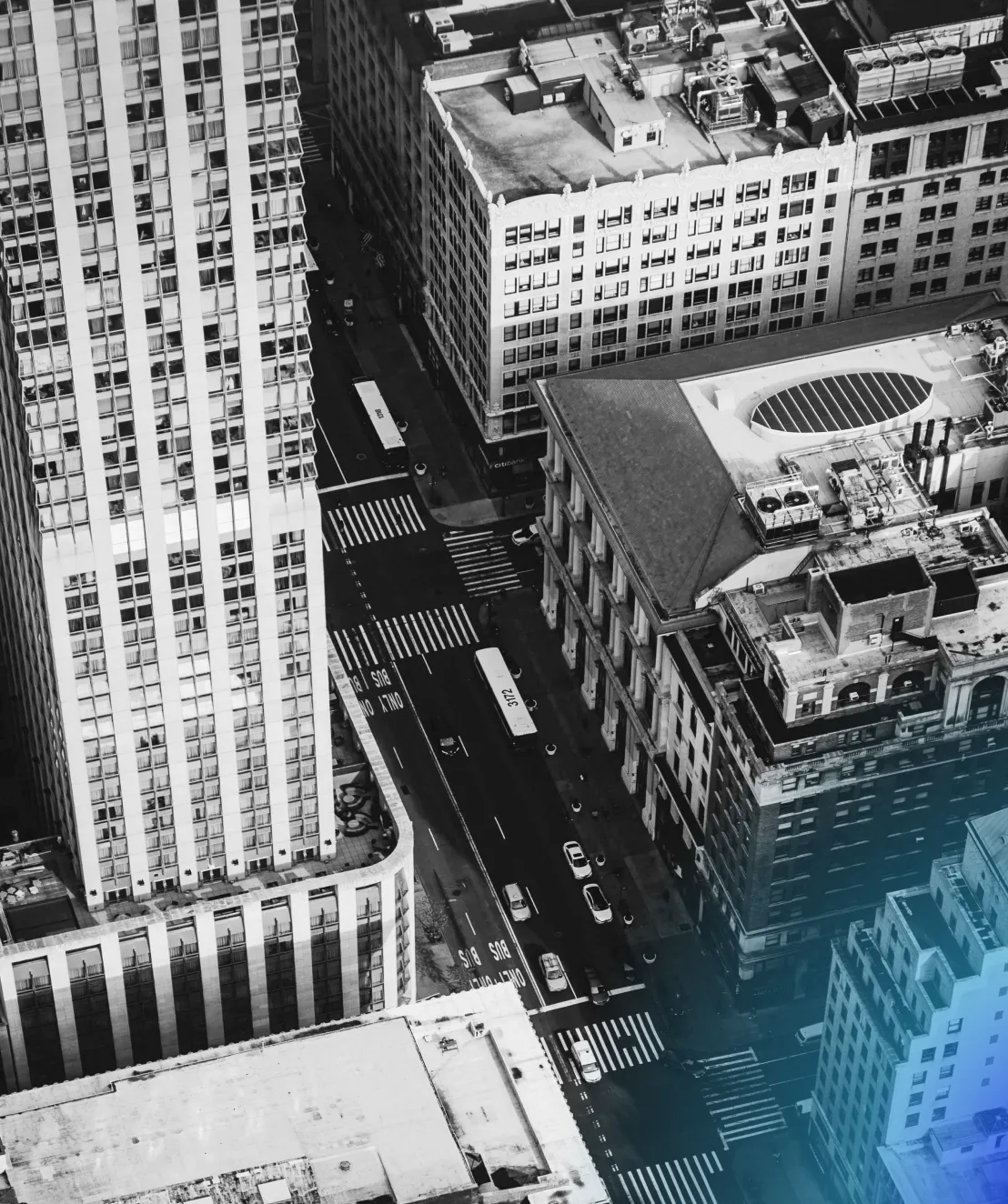 Aerial black-and-white view of a city street with tall buildings, buses, and cars.