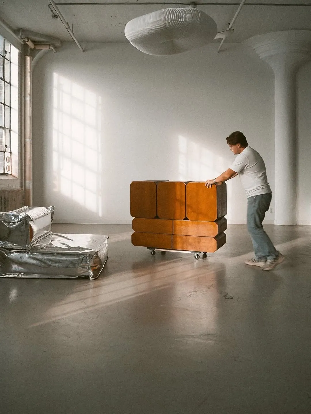 A mover wheeling a wooden cabinet across a sunlit empty room
