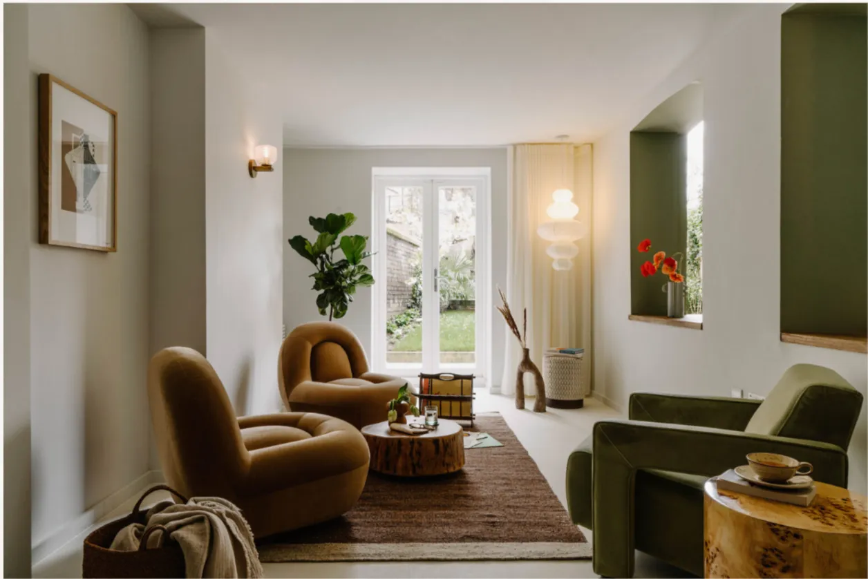 A living room with caramel armchairs and French doors to a garden