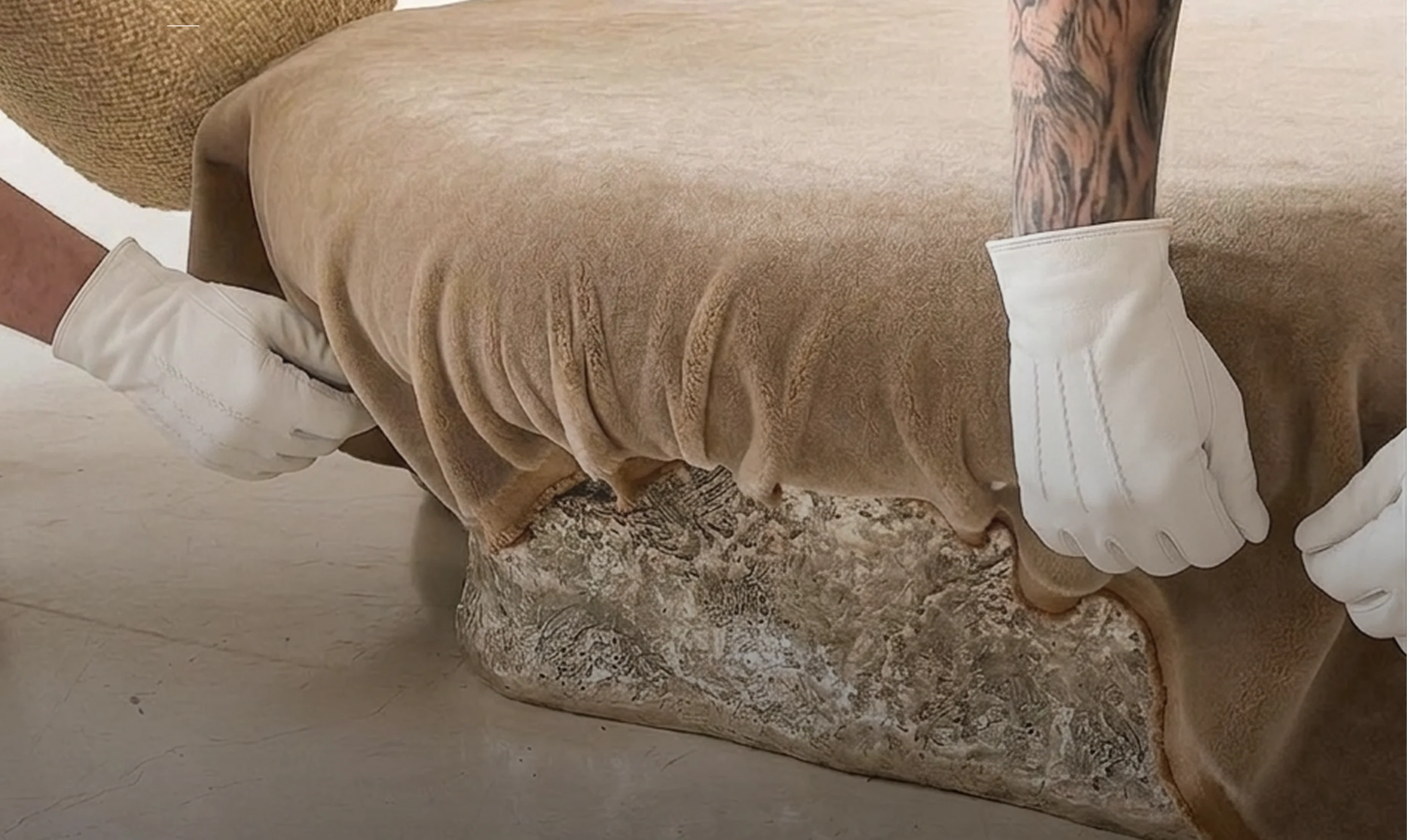 White-gloved Yugo hands wrapping an upholstered ottoman in protective velvet