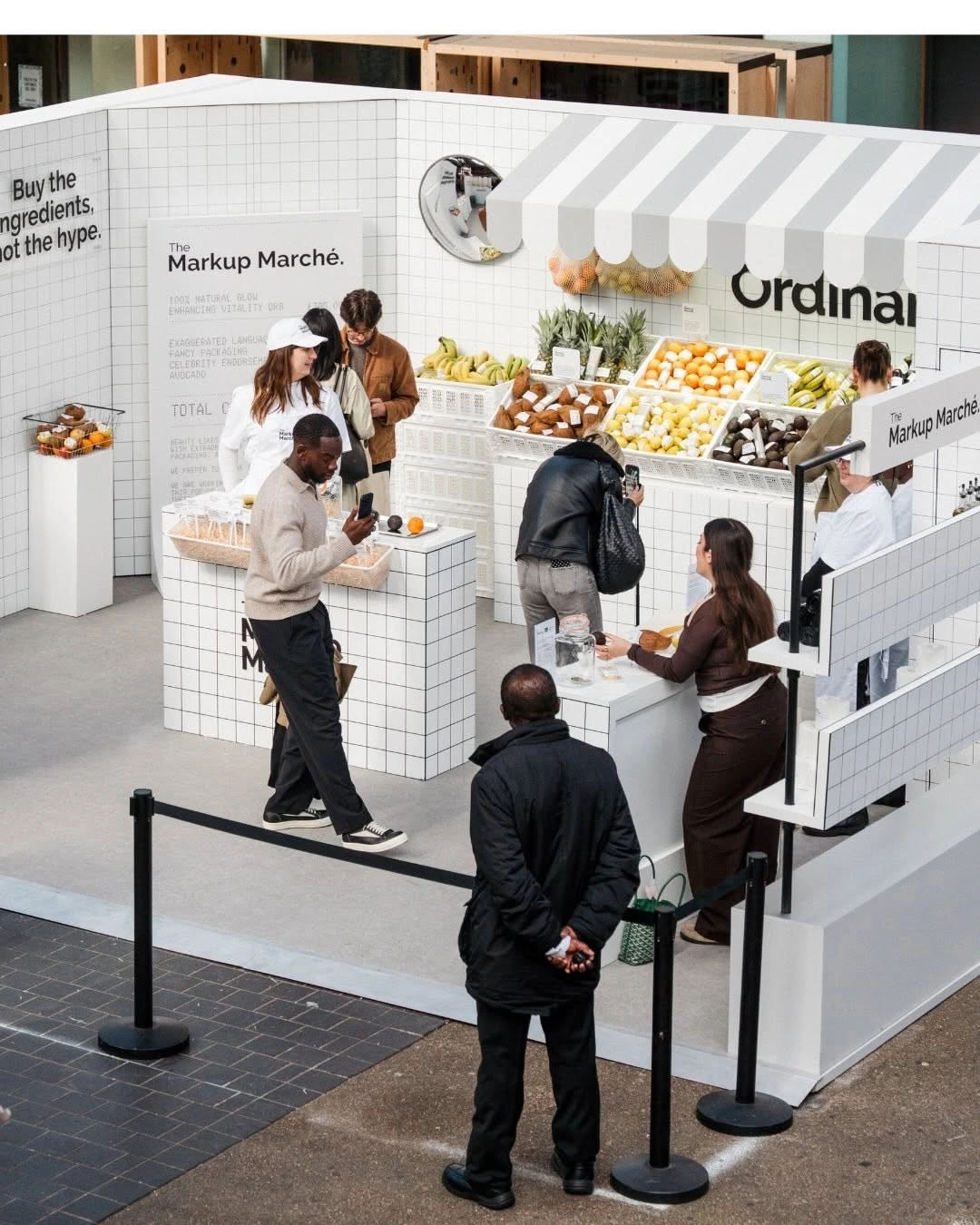 A white pop-up retail kiosk with produce displays and visitors at a brand activation