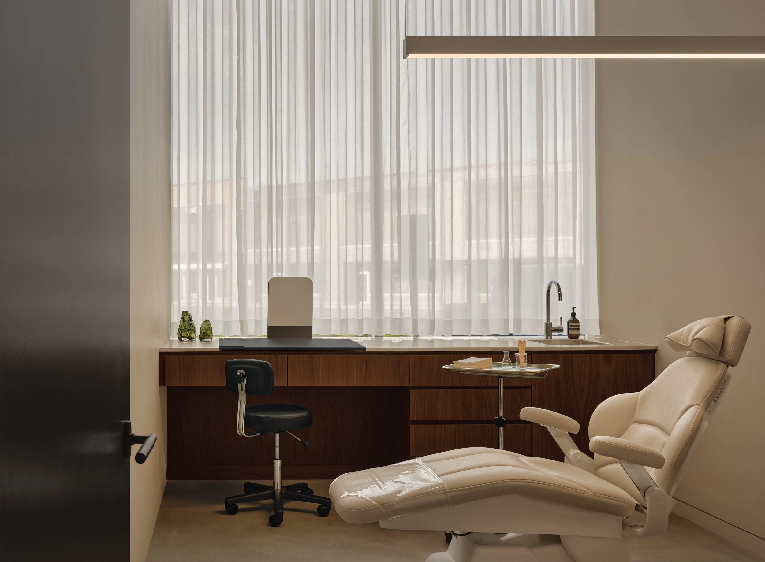 A bright clinic treatment room with a reclining chair and walnut desk