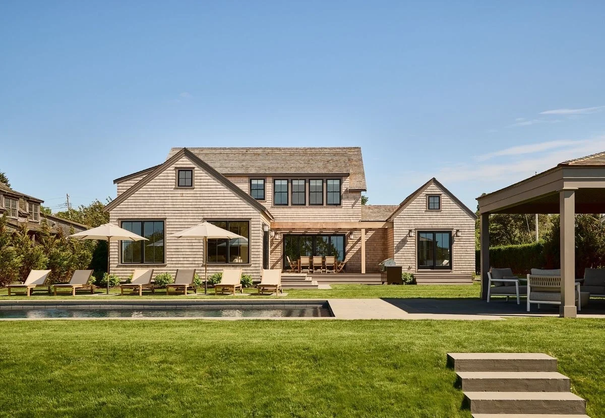 A shingle-style family house with a pool and wide lawn