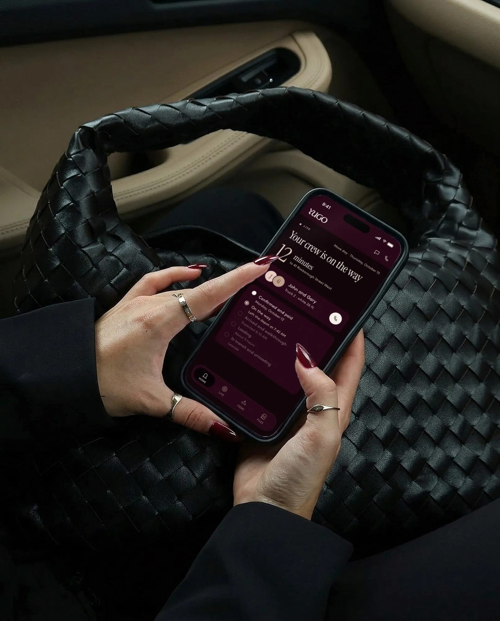 A hand holding a phone with Yugo live move tracking: the crew is 12 minutes from 41 Roxborough Street West, with each move-day step shown
