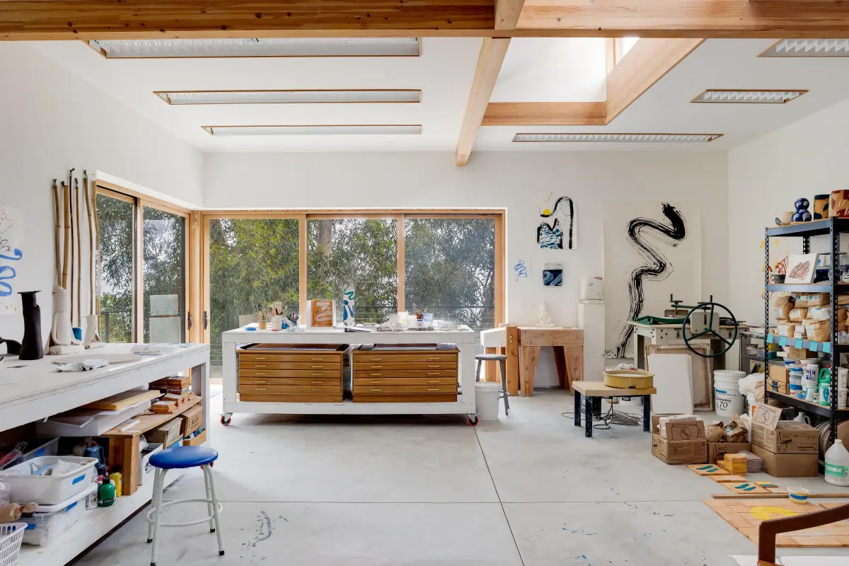 A bright artist's studio with long work tables, shelving and garden windows