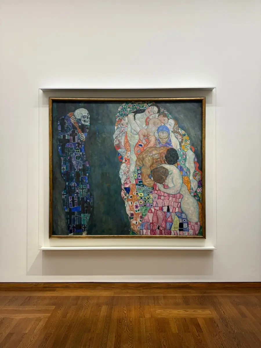 A large gilt-framed painting hung on a white wall above a dark wood floor