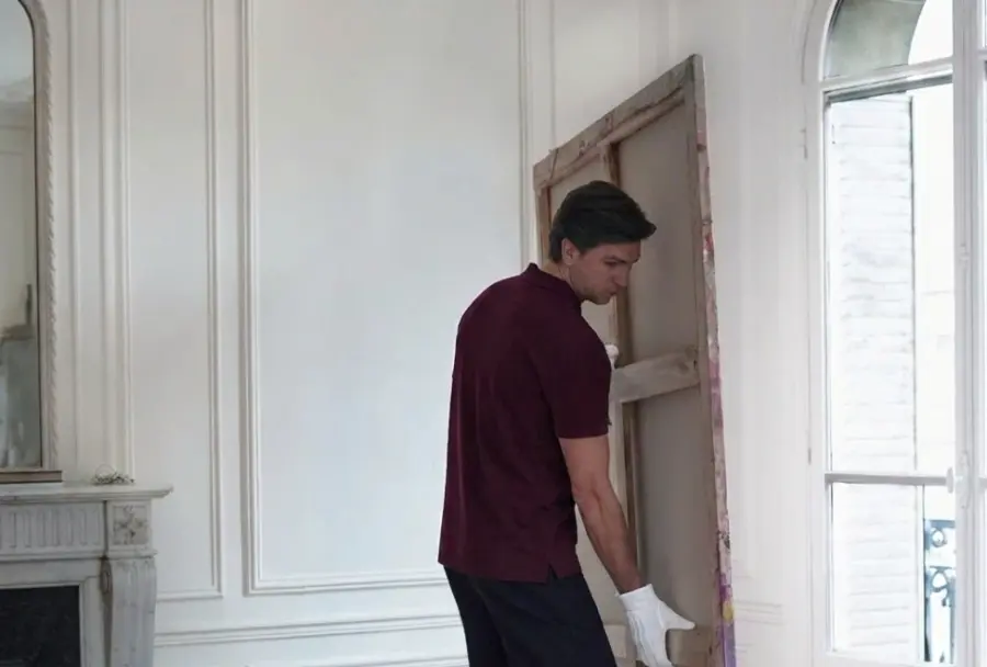 A Yugo specialist in white gloves carrying a large canvas into a client's room