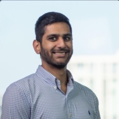 Smiling man with short hair and beard wearing a checkered shirt against a blurry light background.