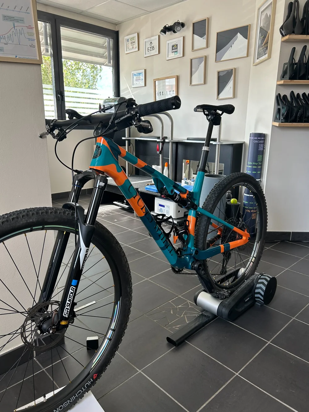 VTT tout suspendu orange et bleu sur home trainer dans l’espace de bikefitting de Belledonne Podologie, près de Grenoble.