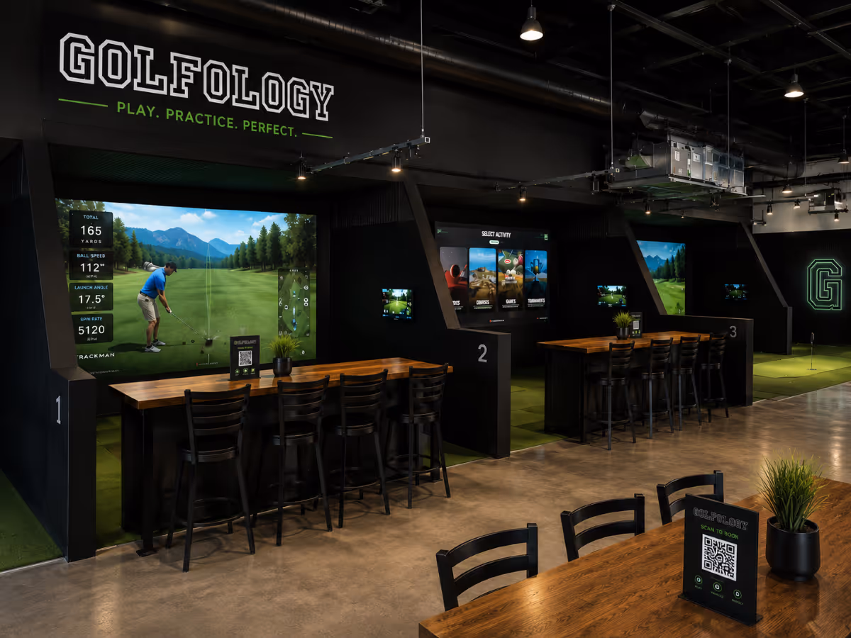 Indoor golf simulators with wooden seating, digital screens, and Golfology branding on the wall.