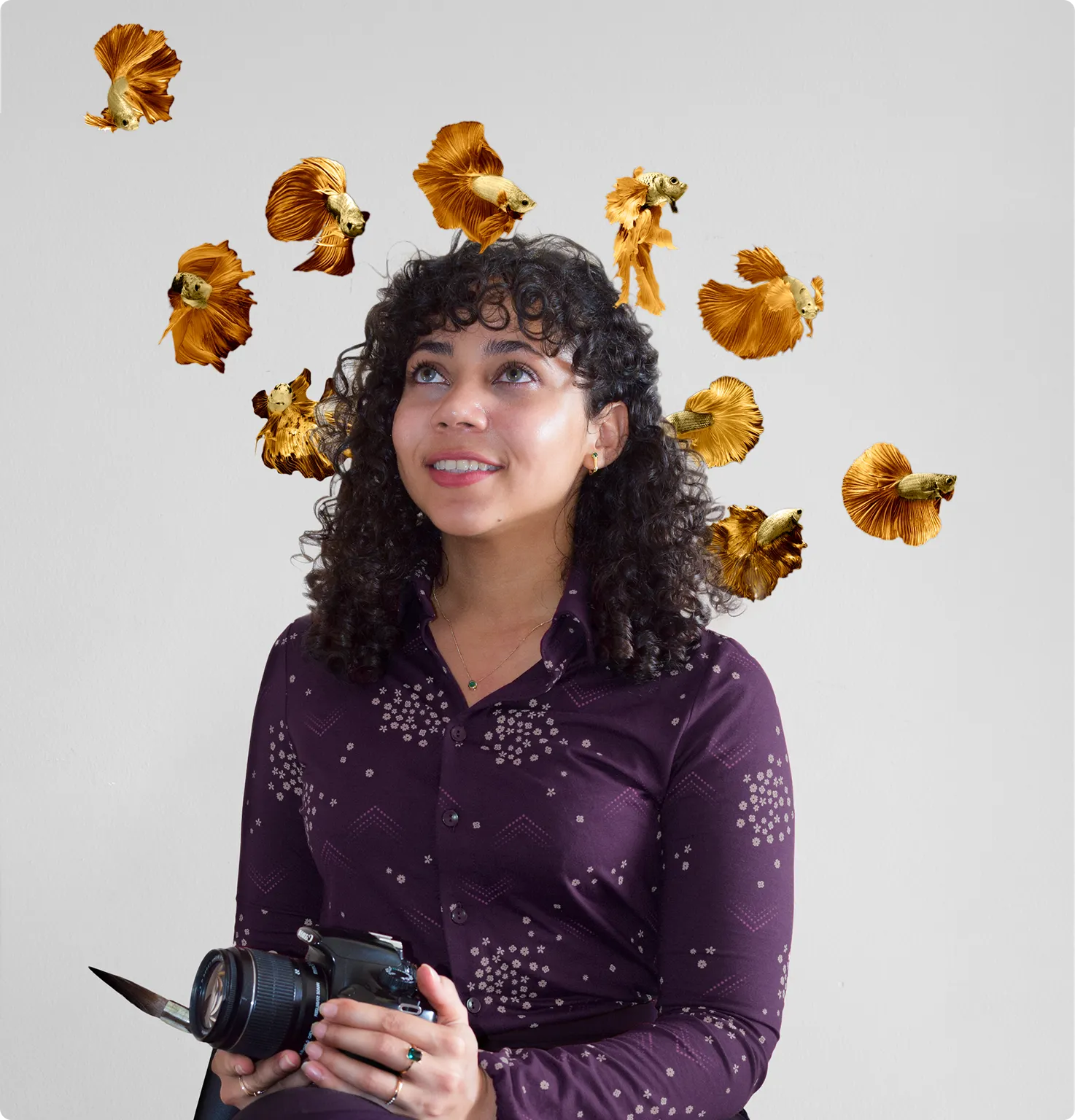 Smiling Nohely with curly hair holds a camera with a paintbrush, golden fish around her head.