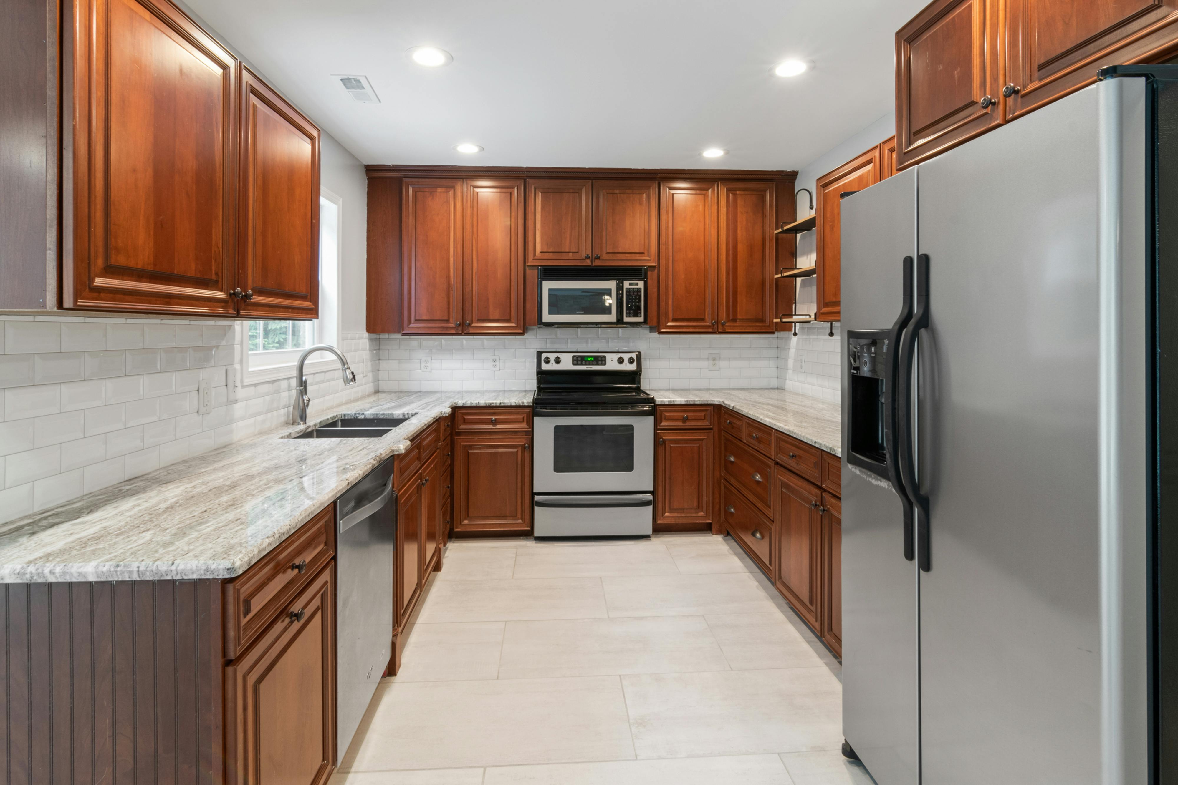 Modern kitchen with wooden cabinets, granite countertops, stainless steel appliances including refrigerator, stove, microwave, and dishwasher.