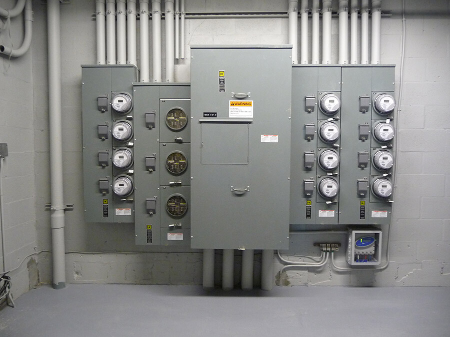 A wall-mounted electrical panel with multiple meters and conduit pipes in a utility room.