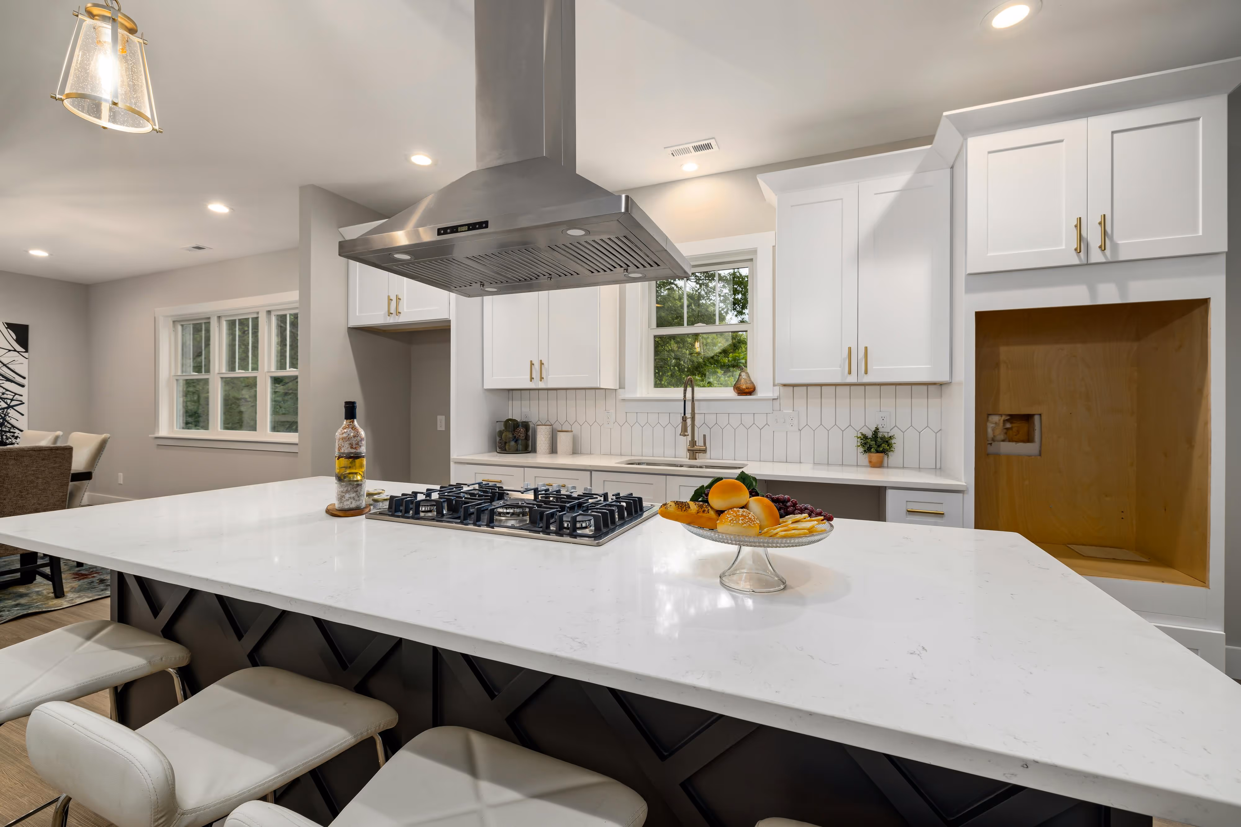 Modern white kitchen with an island, stainless steel appliances, black fixtures, and herringbone tile backsplash.