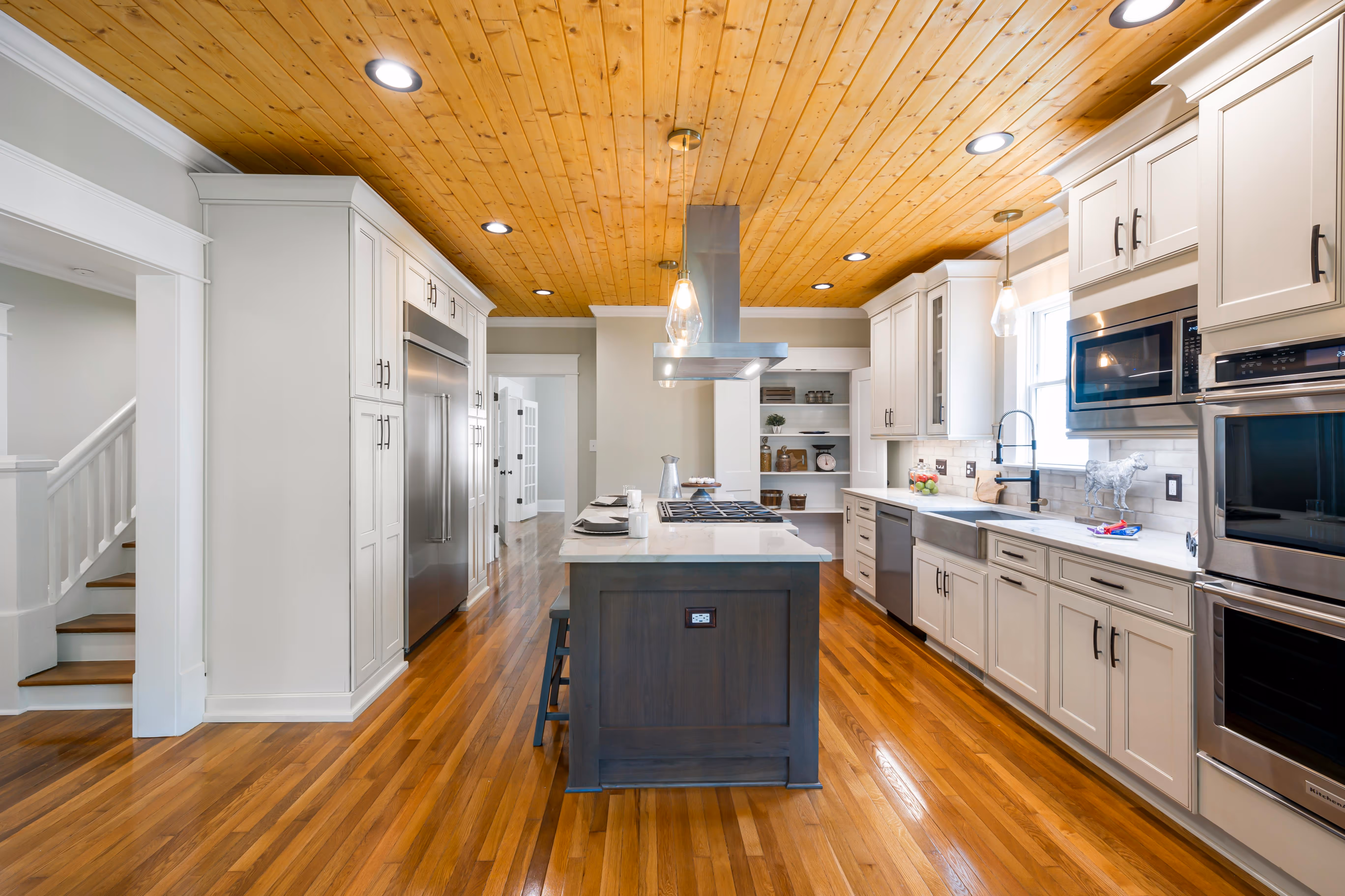 Modern kitchen with light wood cabinets, marble-patterned backsplash, black faucet, induction cooktop, and a bowl of fruit next to a potted plant.