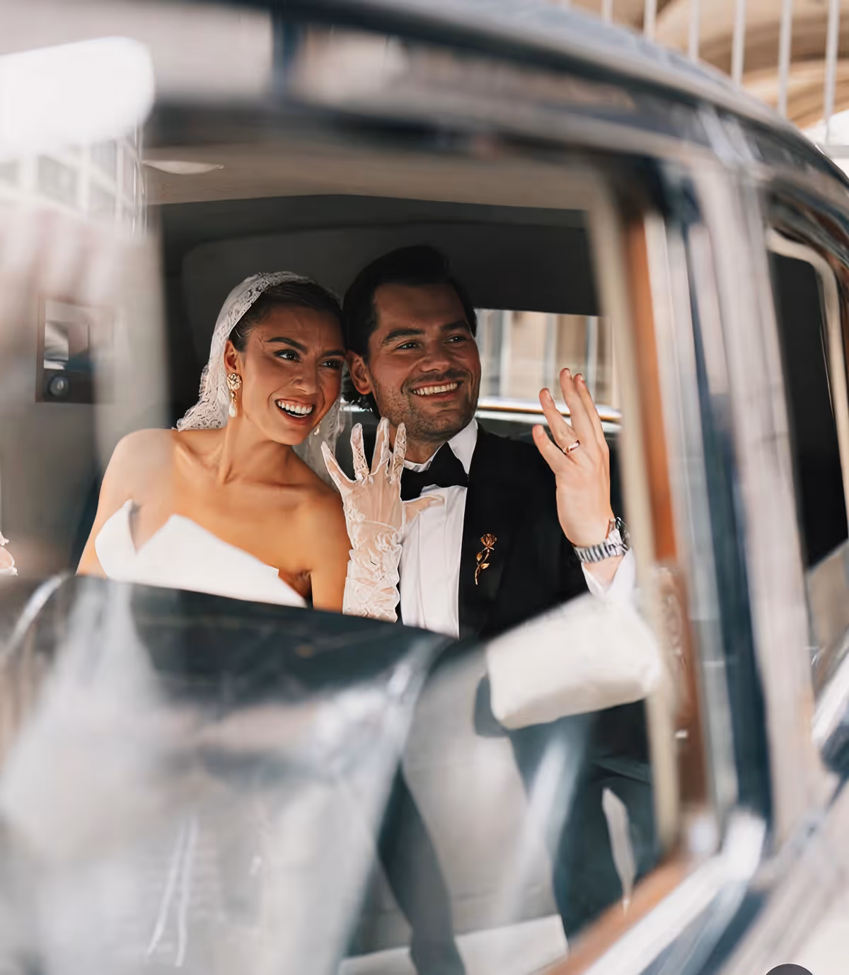Smiling newlywed couple sitting in a car showing their wedding rings.