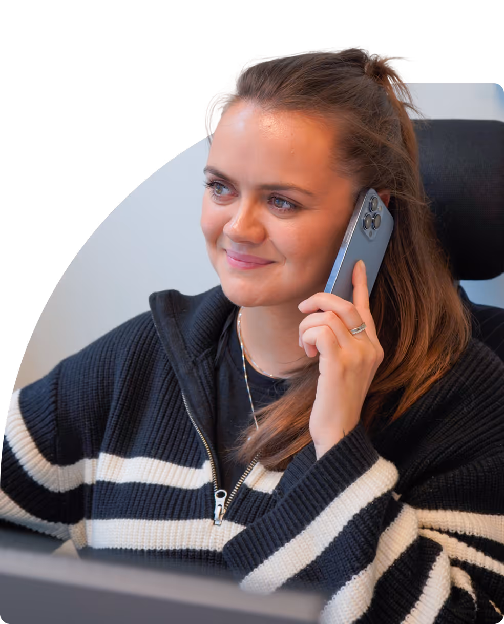 Kvinne som har en telefonsamtale og smiler, iført stripete genser og håret i hestehale.