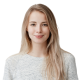 Smiling young woman with long blonde hair wearing a light grey t-shirt against a white background.