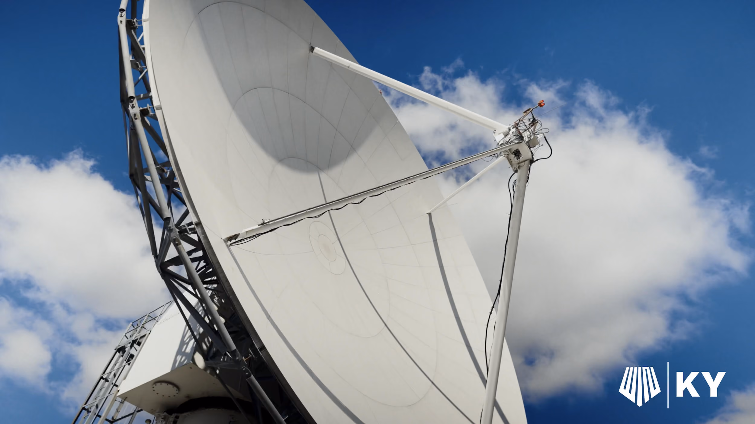 Large white satellite dish antenna against a blue sky with white clouds.