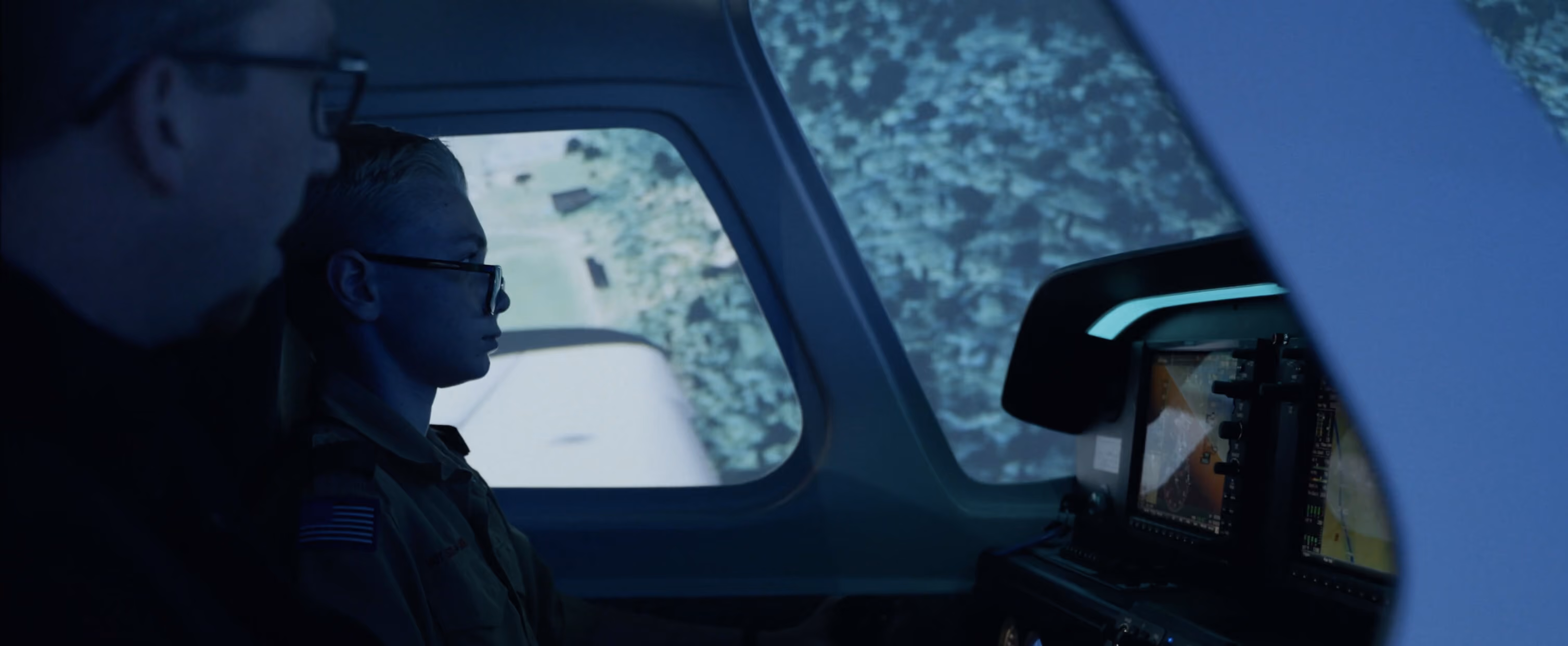Two people inside an aircraft cockpit, one focused on the flight instruments and screens.