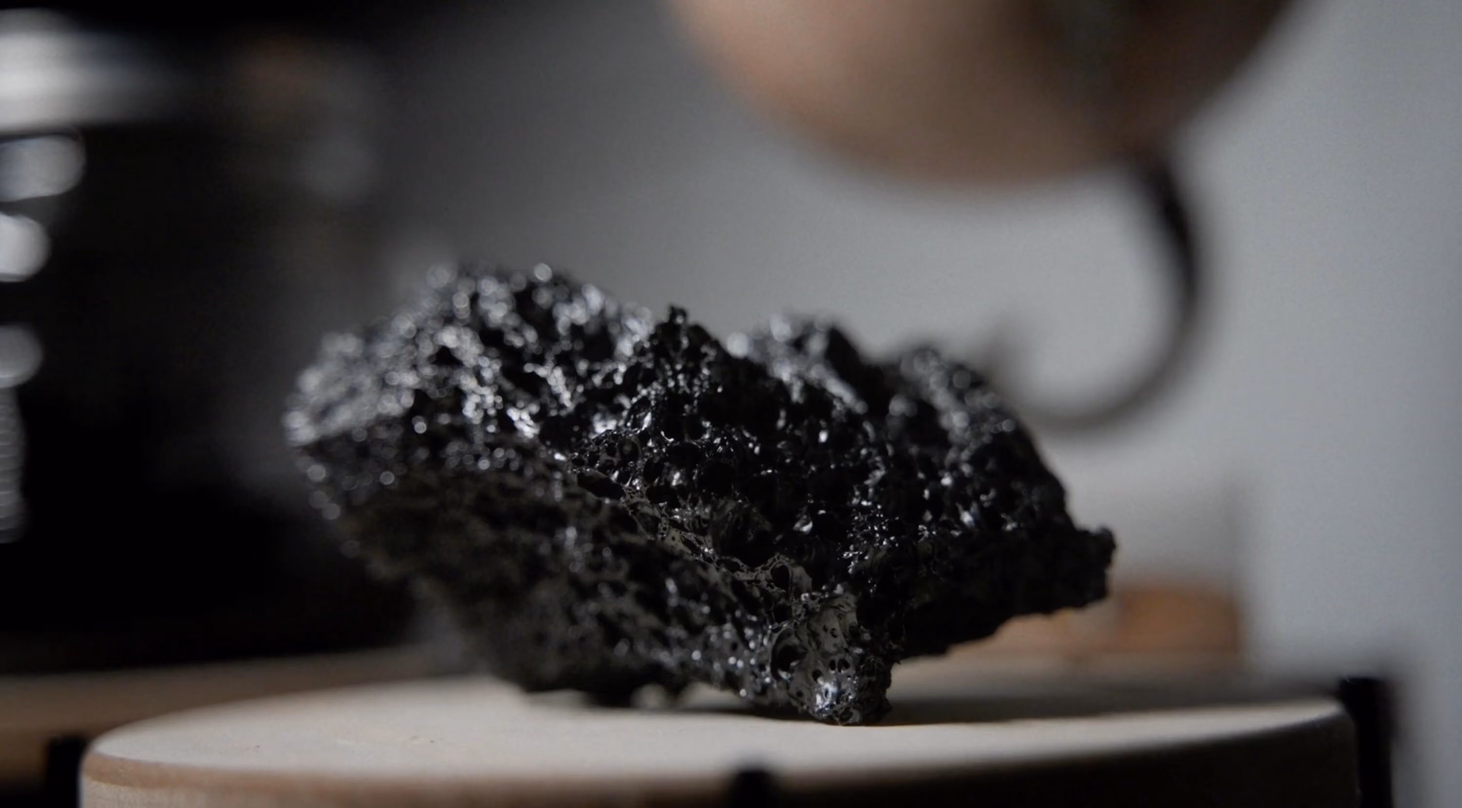 Close-up of shiny black porous volcanic rock on a light wooden surface with blurred background.