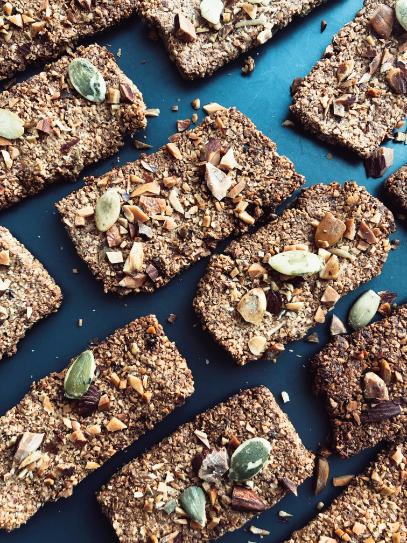 Thin golden seed crackers with pumpkin, sunflower and sesame seeds broken into shards on a board