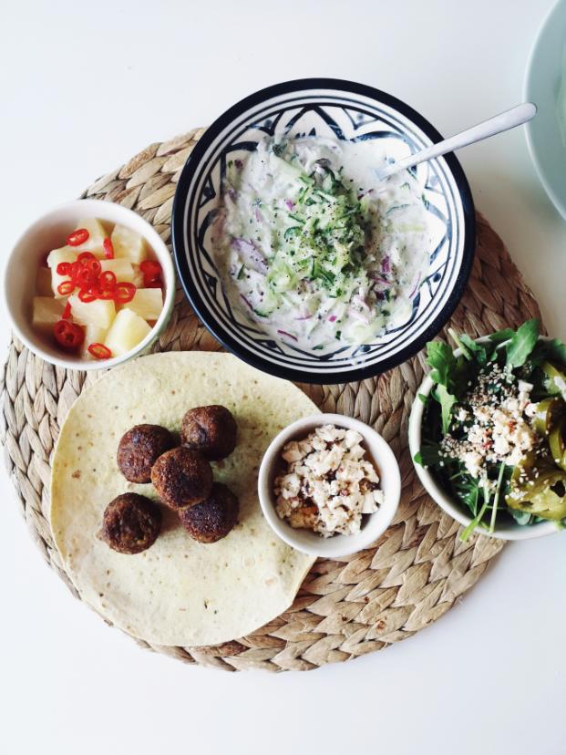 Grilled lamb kofta on skewers with a bowl of tzatziki and a bulgur wheat salad with tomatoes, cucumber and parsley