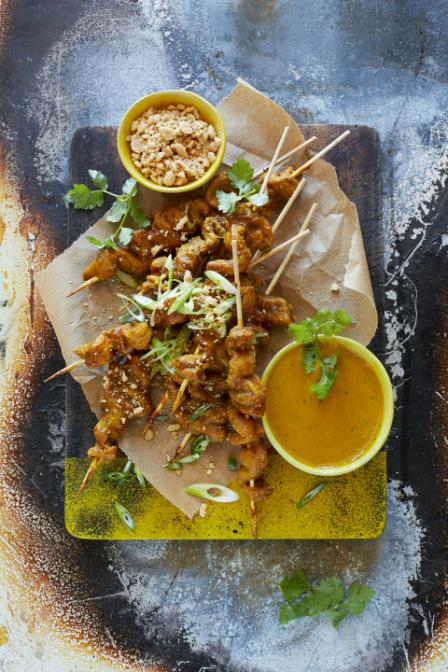 Grilled chicken satay skewers with peanut sauce, a cucumber and red onion salad and lime wedges