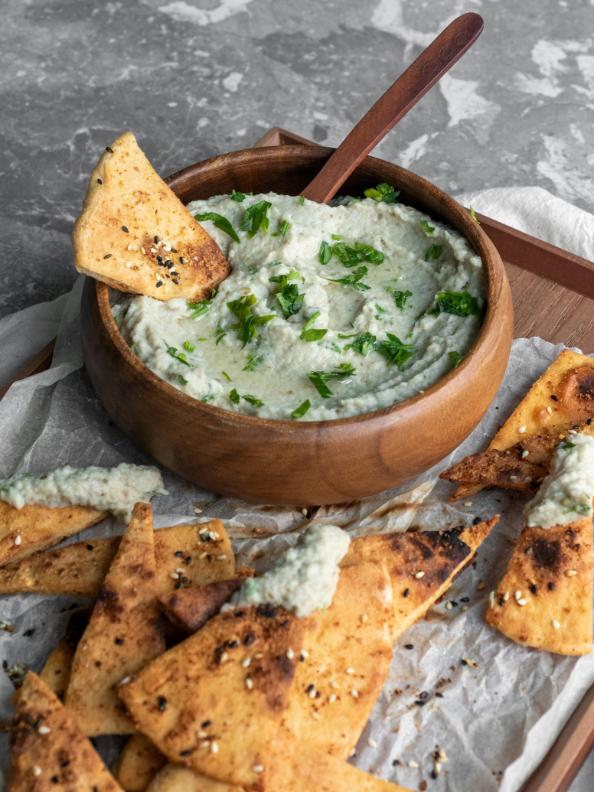 Golden courgette and feta fritters on a plate with a bowl of lemon and garlic yogurt dip and fresh herbs