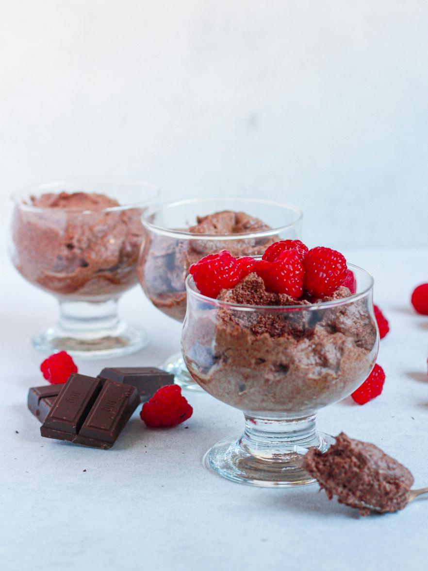 Glasses of chocolate avocado mousse topped with fresh raspberries and a sprinkle of cocoa