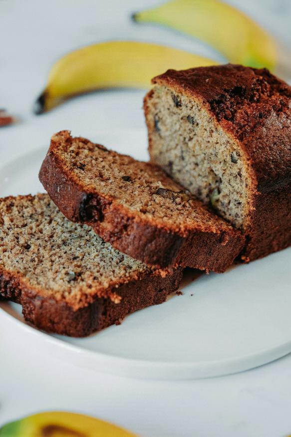 Sliced loaf of healthy banana bread topped with walnuts and banana, on a wooden board