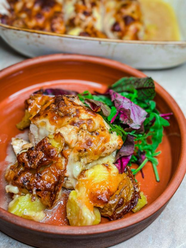 A roasting tray of harissa chicken thighs with browned cauliflower, chickpeas and red onion, with a bowl of lemon yogurt and parsley