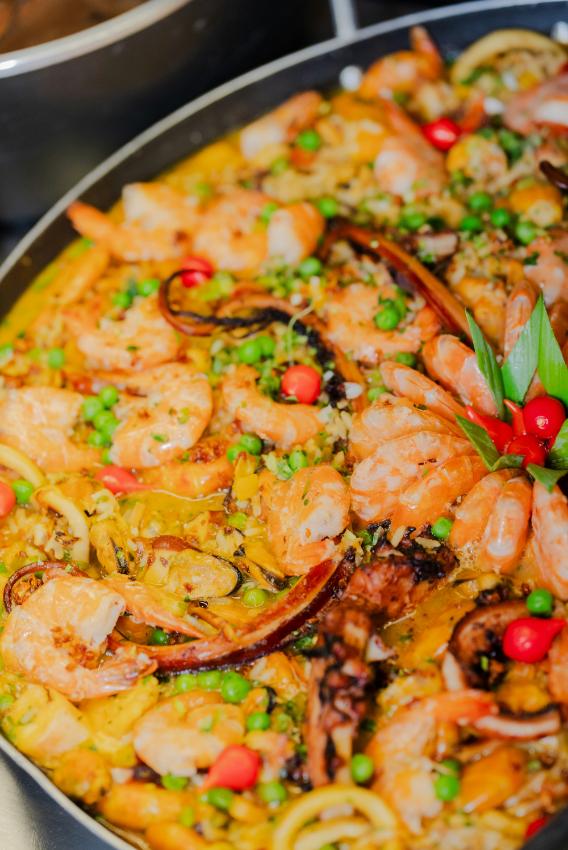 A wide paella pan of golden saffron rice with king prawns, red pepper, green beans, peas, lemon wedges and parsley