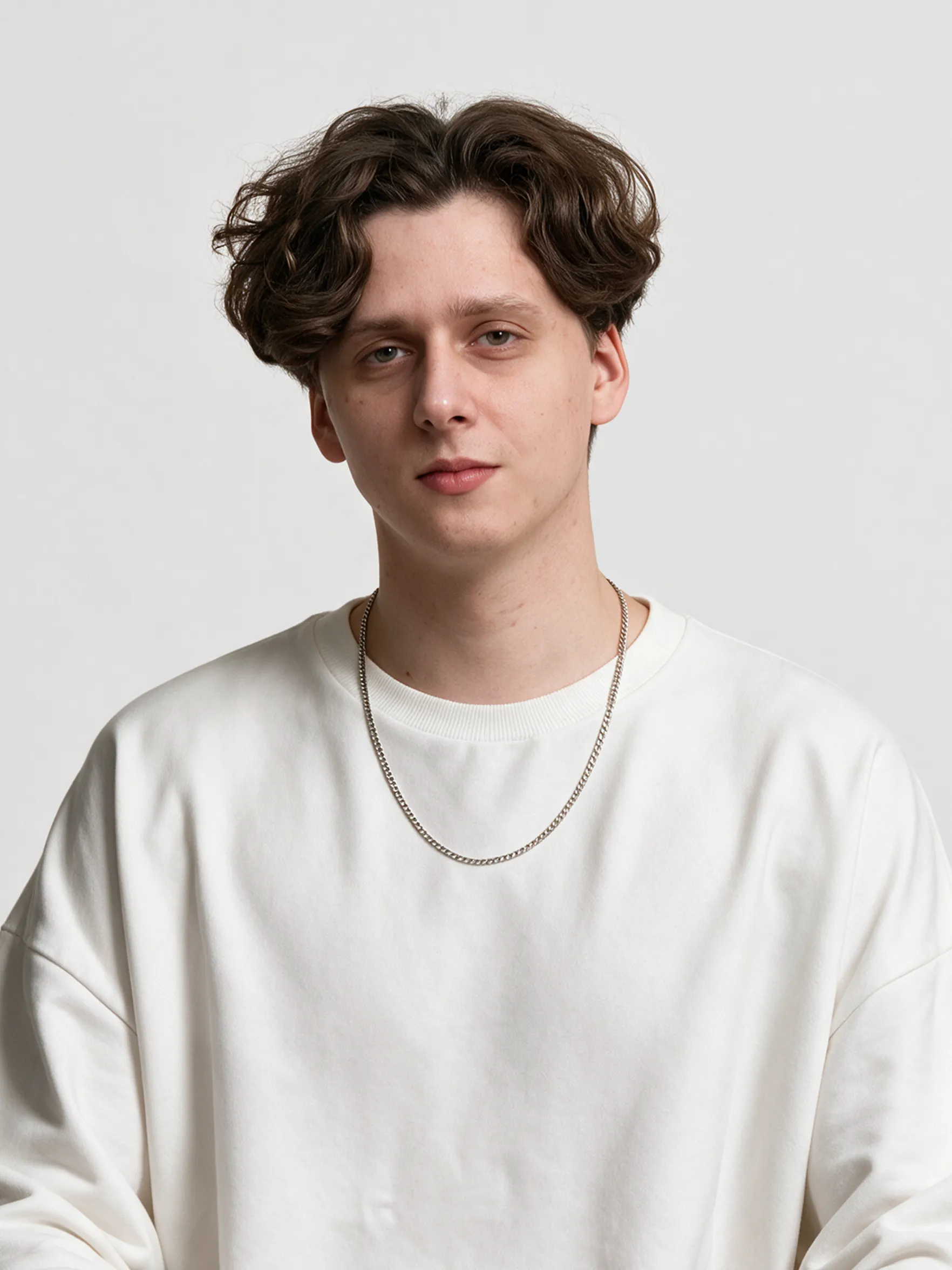 Portrait of a young man with wavy brown hair and a silver chain