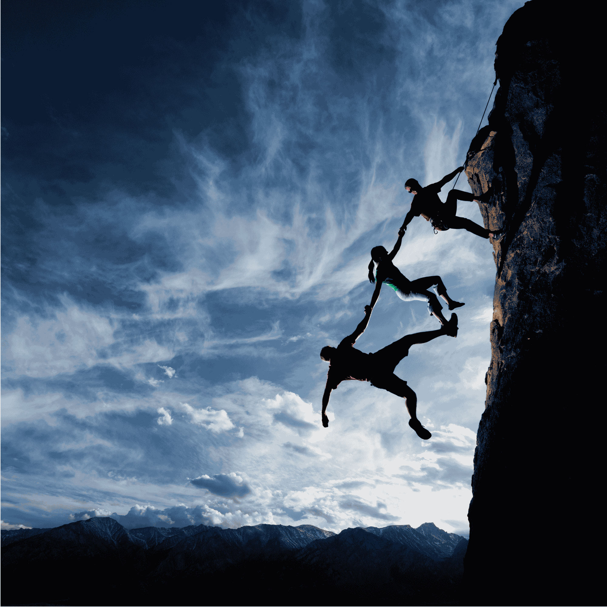 Three climbers share hands while climbing a rock face against a dramatic blue sky and mountains.