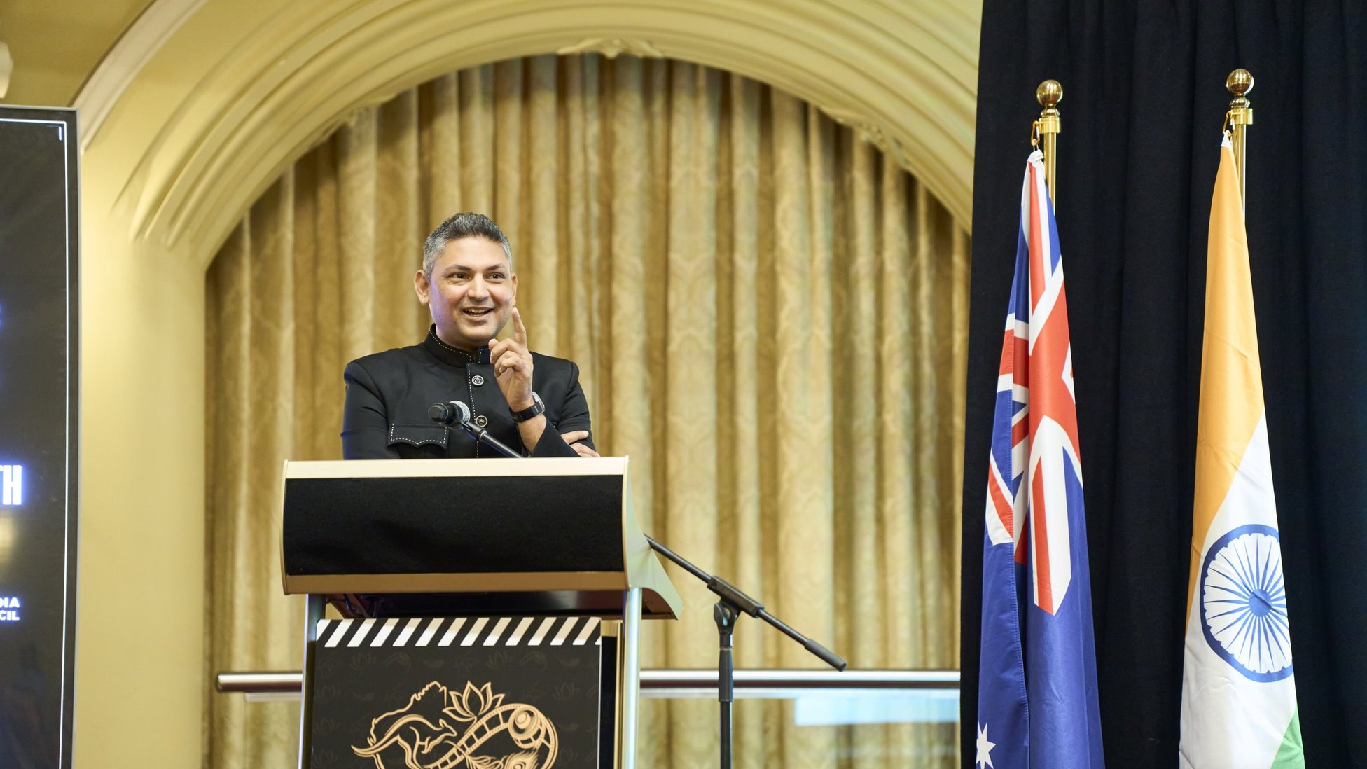 Nilesh Makwana smiling at the lectern beside the Australian and Indian flags