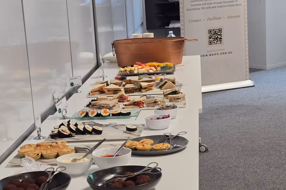 Long table with assorted sandwiches, sushi, dips, snacks, and a copper tub for drinks.