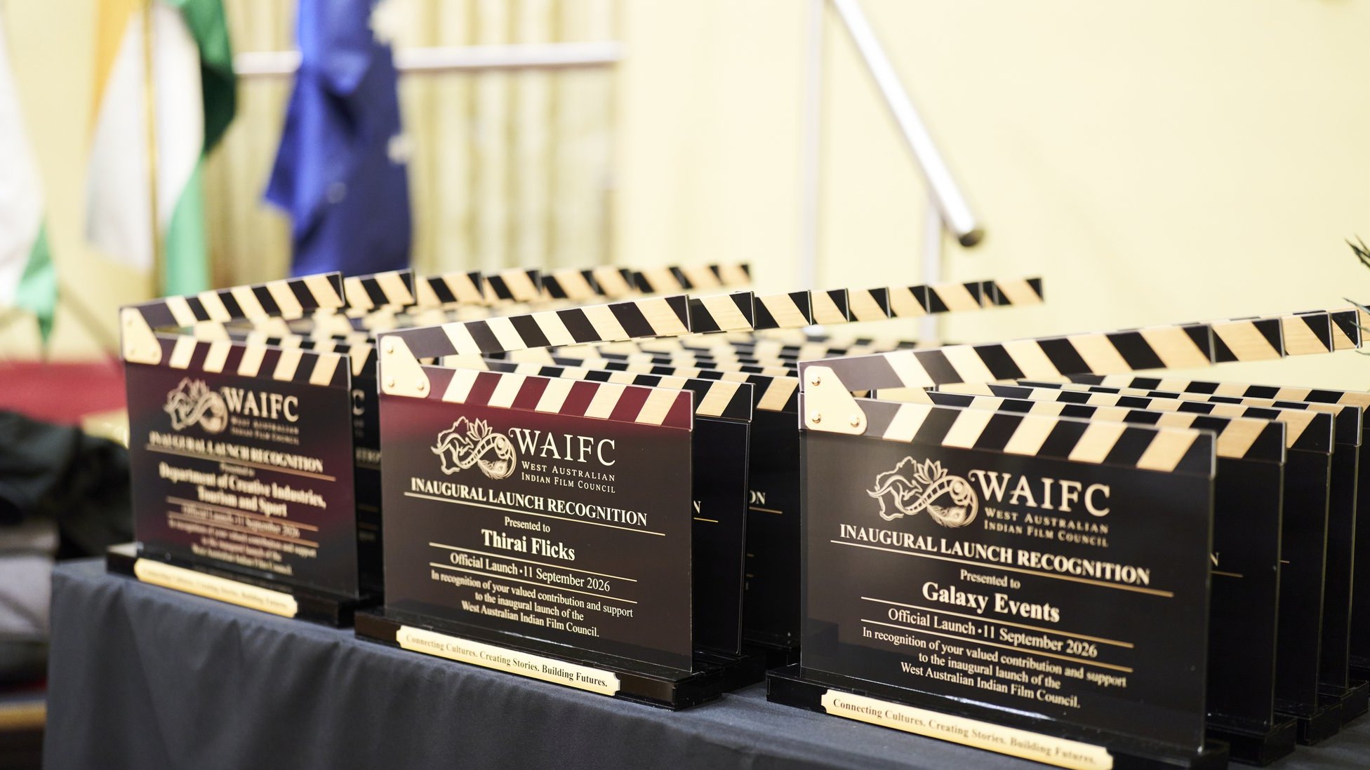 Black and gold WAIFC inaugural launch recognition clapperboards lined up on a table, each engraved with a partner's name