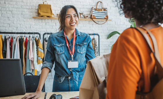 Smiling retail worker in denim shirt assisting customer in orange coat inside clothing store.