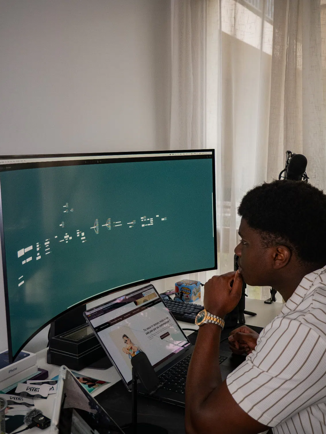 Homme en chemise rayée se concentrant sur un grand écran incurvé affichant une interface logicielle au bureau.